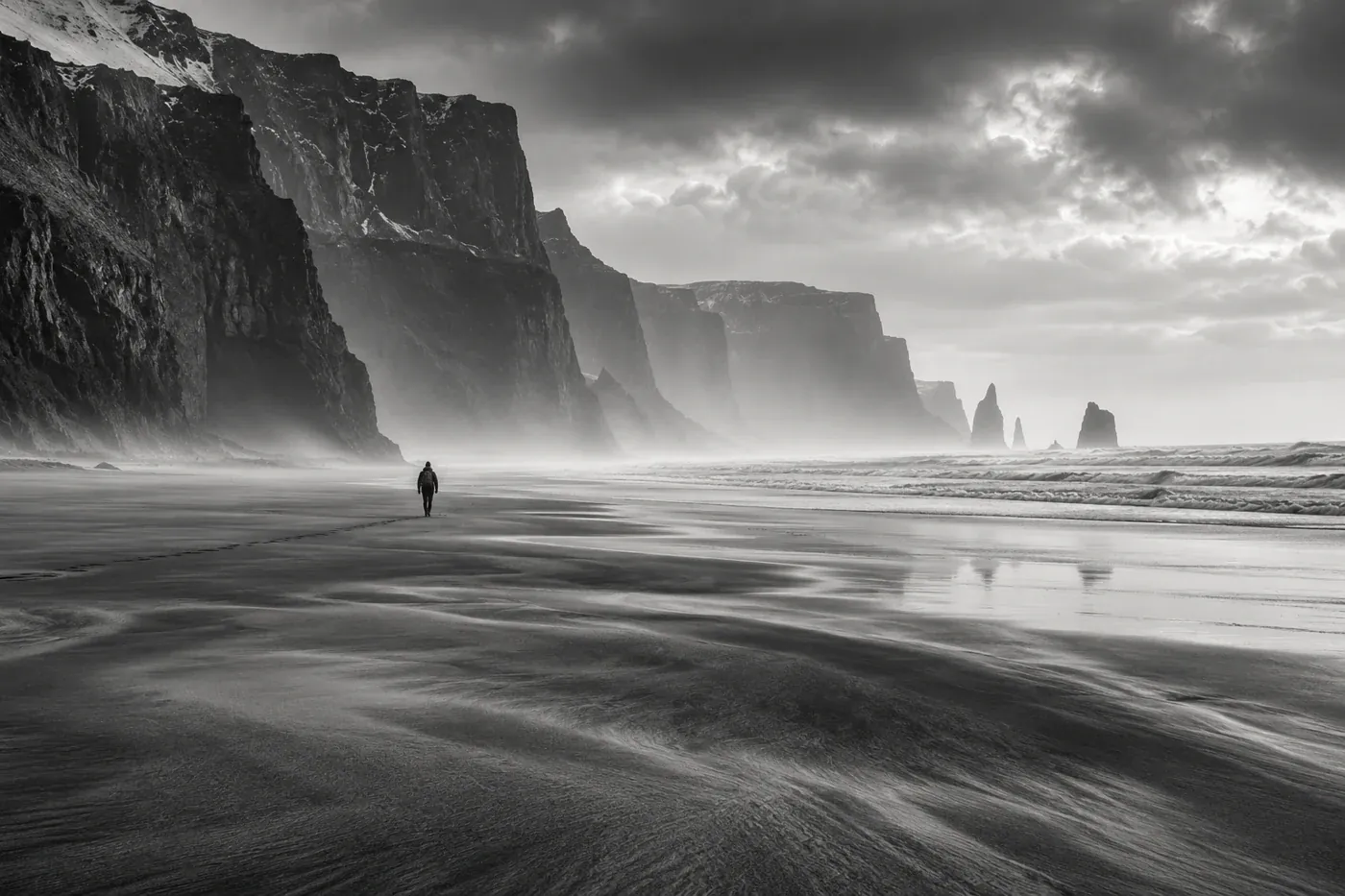 A person on a wide beach below coastal cliffs